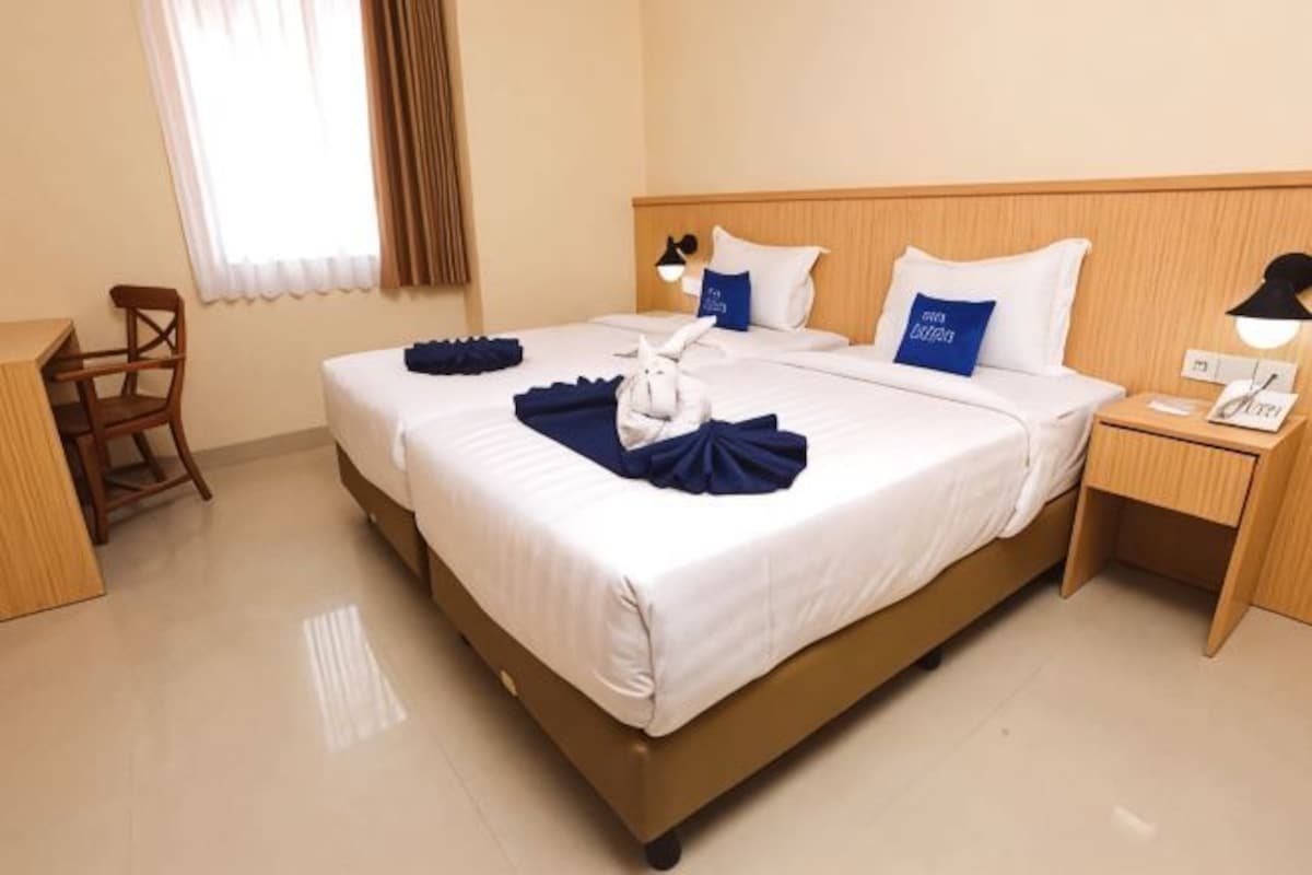 Habitación de hotel con una cama grande, dos mesitas de noche, una silla y una ventana con cortinas.