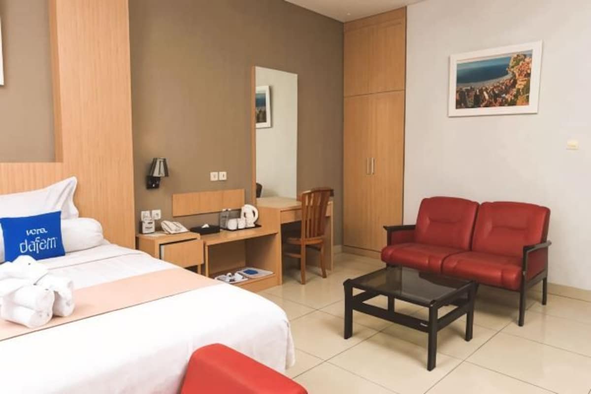 Una habitación de hotel con cama, escritorio, silla, sofá rojo y una mesita de centro.