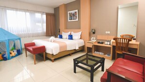 Une chambre d’hôtel avec un lit, un bureau, une chaise, une petite table, un canapé rouge, une tente de jeu bleue et un grand miroir.