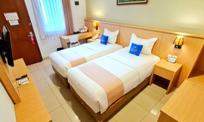 A hotel room with two beds, a desk, a chair, a telephone, and a lamp.