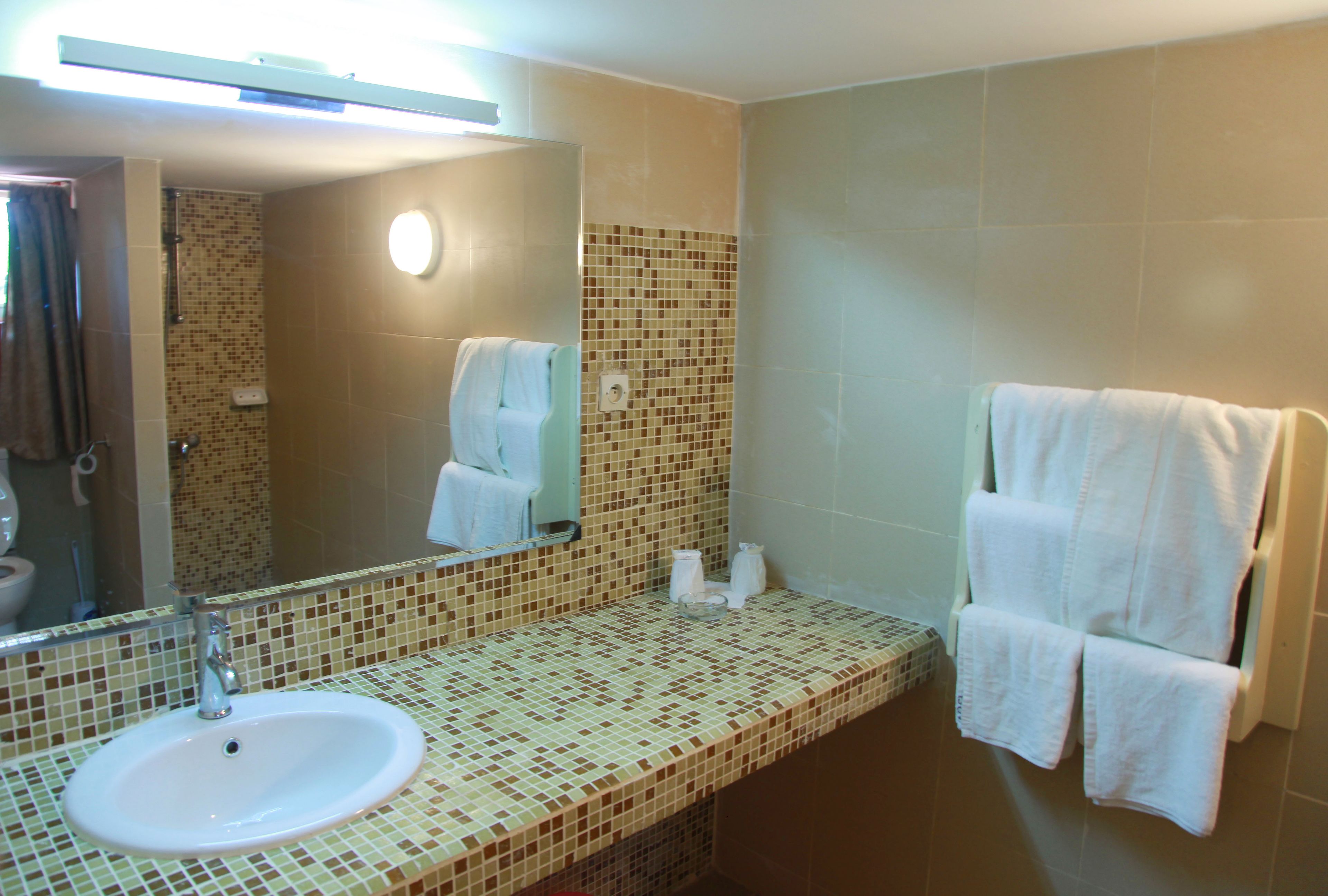 A bathroom with a tiled sink, mirror, and towel rack.