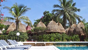 A poolside area with lounge chairs, a stone wall, and thatched umbrellas.
