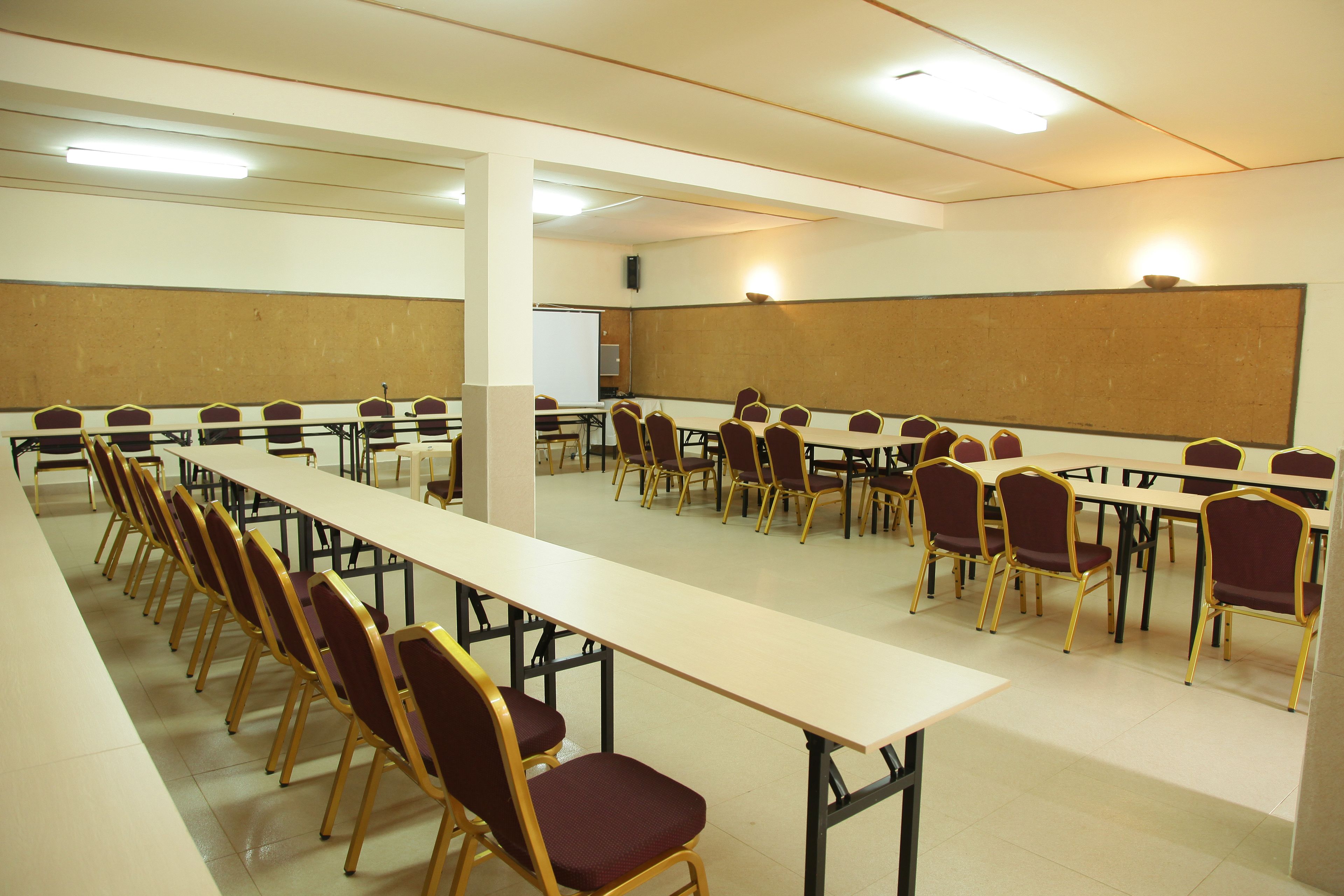 A conference room with long tables and chairs, a whiteboard, and a projector screen.