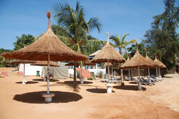 A beach area with thatched umbrellas and lounge chairs. - Hôtel Les Bougainvillées Saly Sénégal (Mbour)