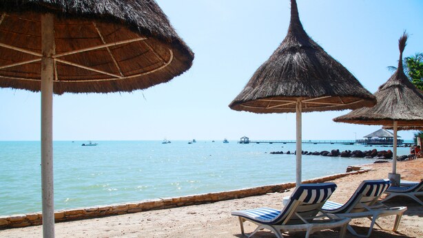 A beach with thatched umbrellas and lounge chairs by the water.