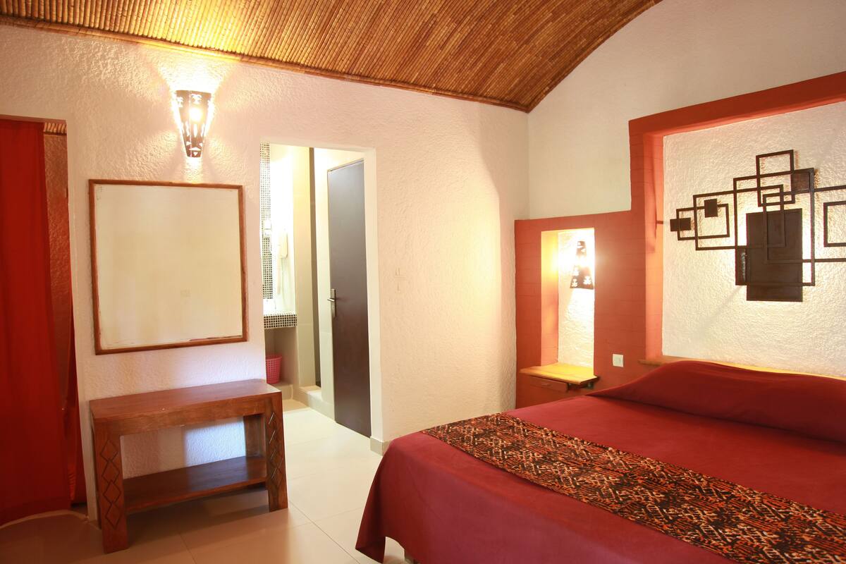 Une chambre d’hôtel avec un grand lit, un banc en bois, un miroir fixé au mur et une œuvre d’art décorative.