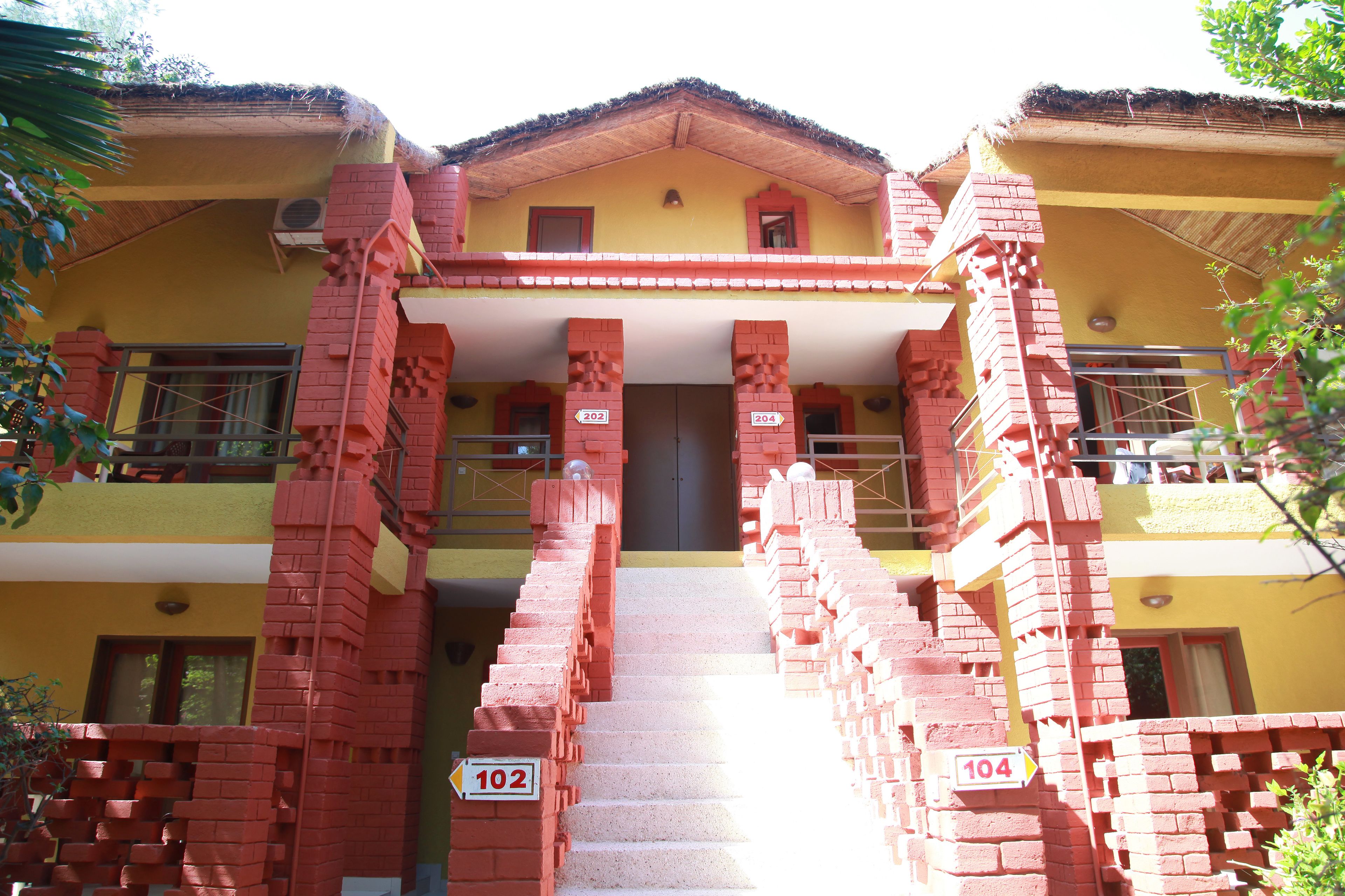 A building with a yellow facade, red brick staircases, and numbered signs indicating room numbers 102 and 104.