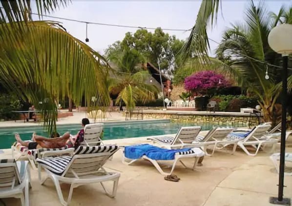 A poolside area with lounge chairs and a swimming pool, surrounded by palm trees and tropical plants. - Hôtel Les Bougainvillées Saly Sénégal (Mbour)