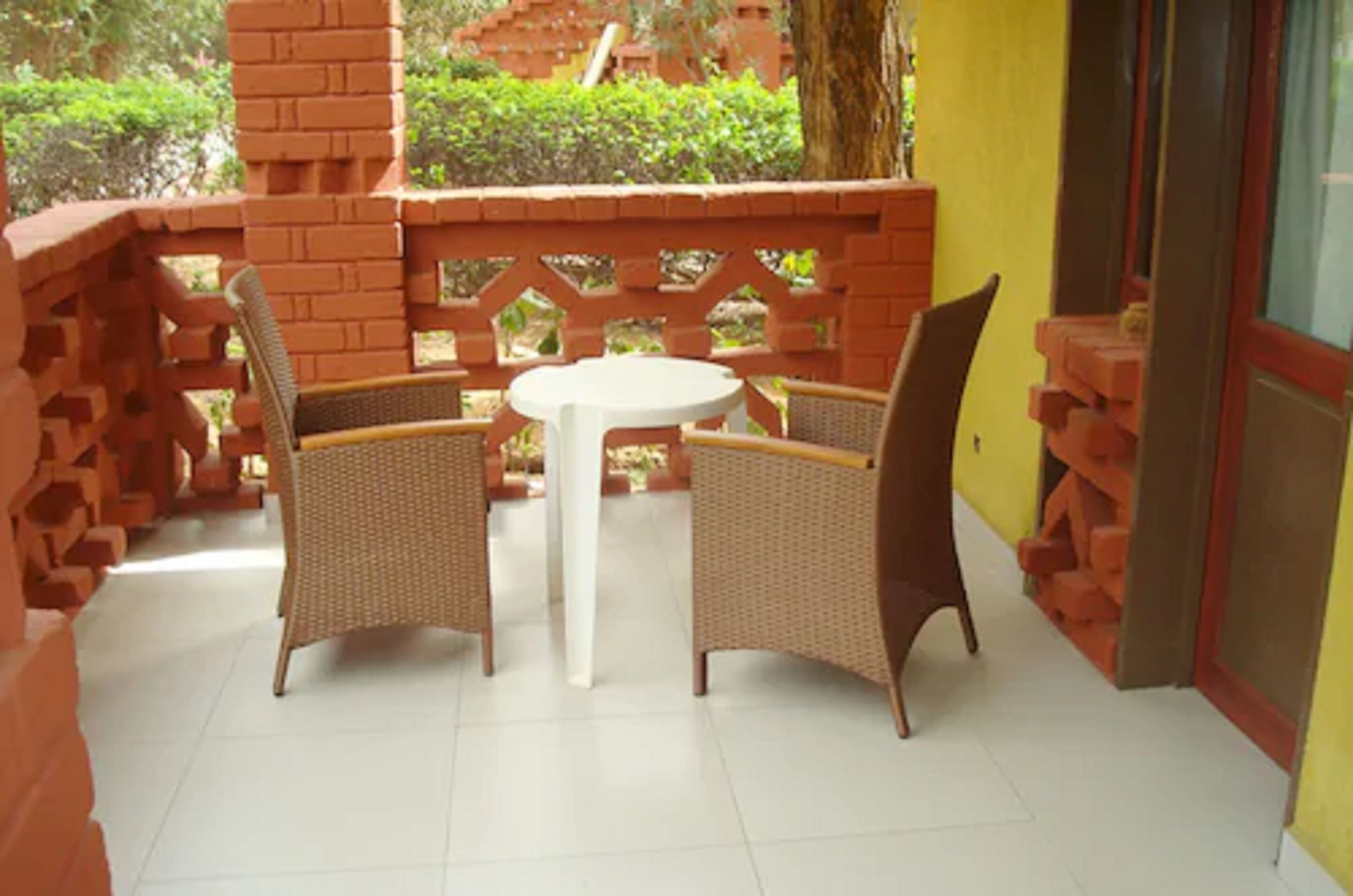 A patio area with wicker furniture and a white table, surrounded by brick walls and a glass door.