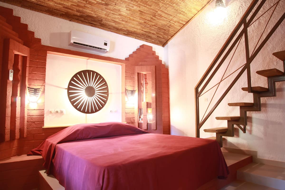 Une chambre avec un lit, un luminaire circulaire fixé au mur, un escalier et un mur en briques.