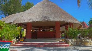 A thatched-roof pavilion with a red and beige color scheme, surrounded by potted plants and a stone wall.