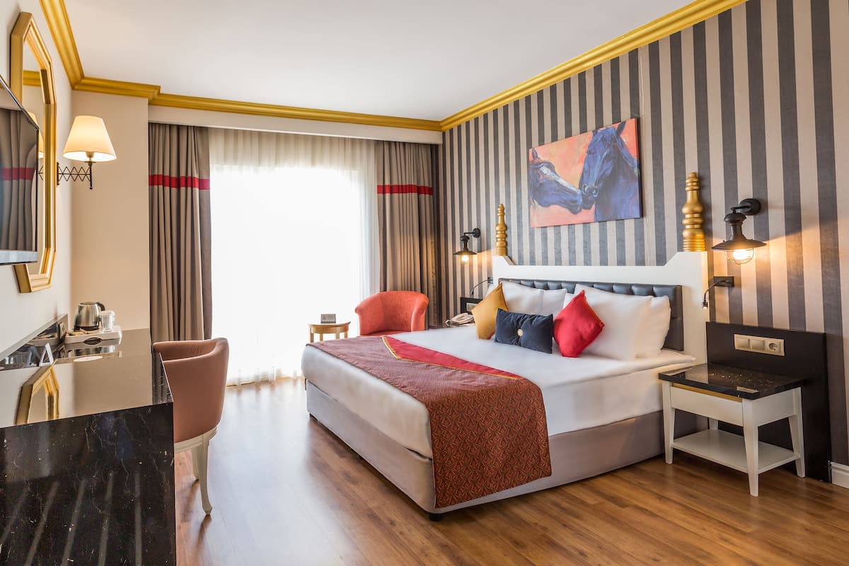 A hotel room with a large bed, a desk, a chair, a nightstand, and a painting on the wall.