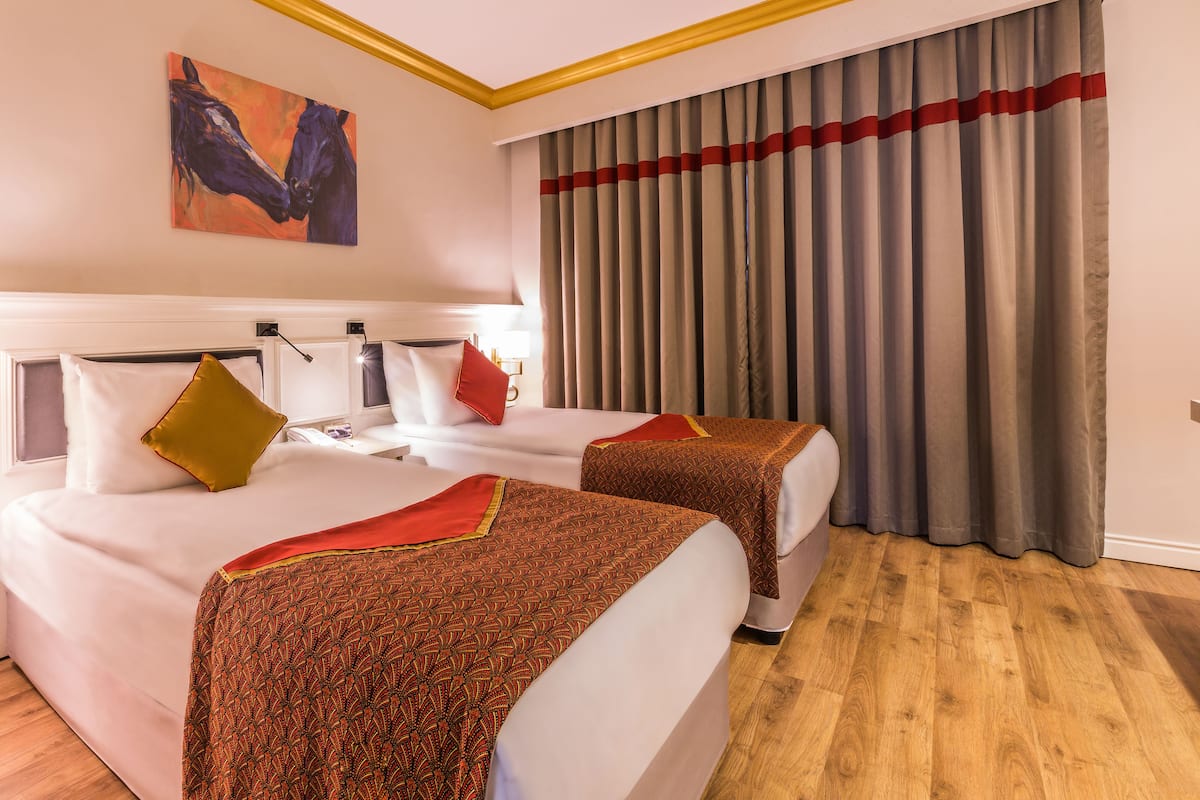 A hotel room with two beds, a painting on the wall, and a large window with curtains.