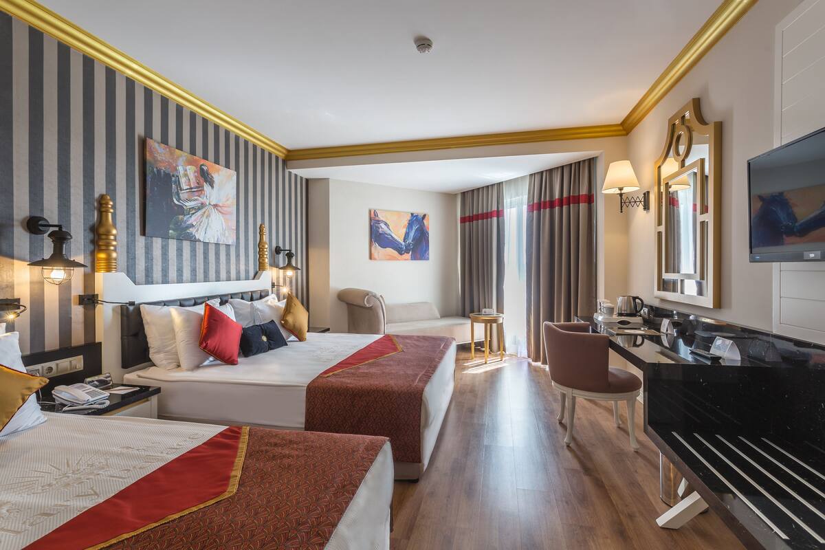 A hotel room with two beds, a sofa, a desk with a TV, and a piano.