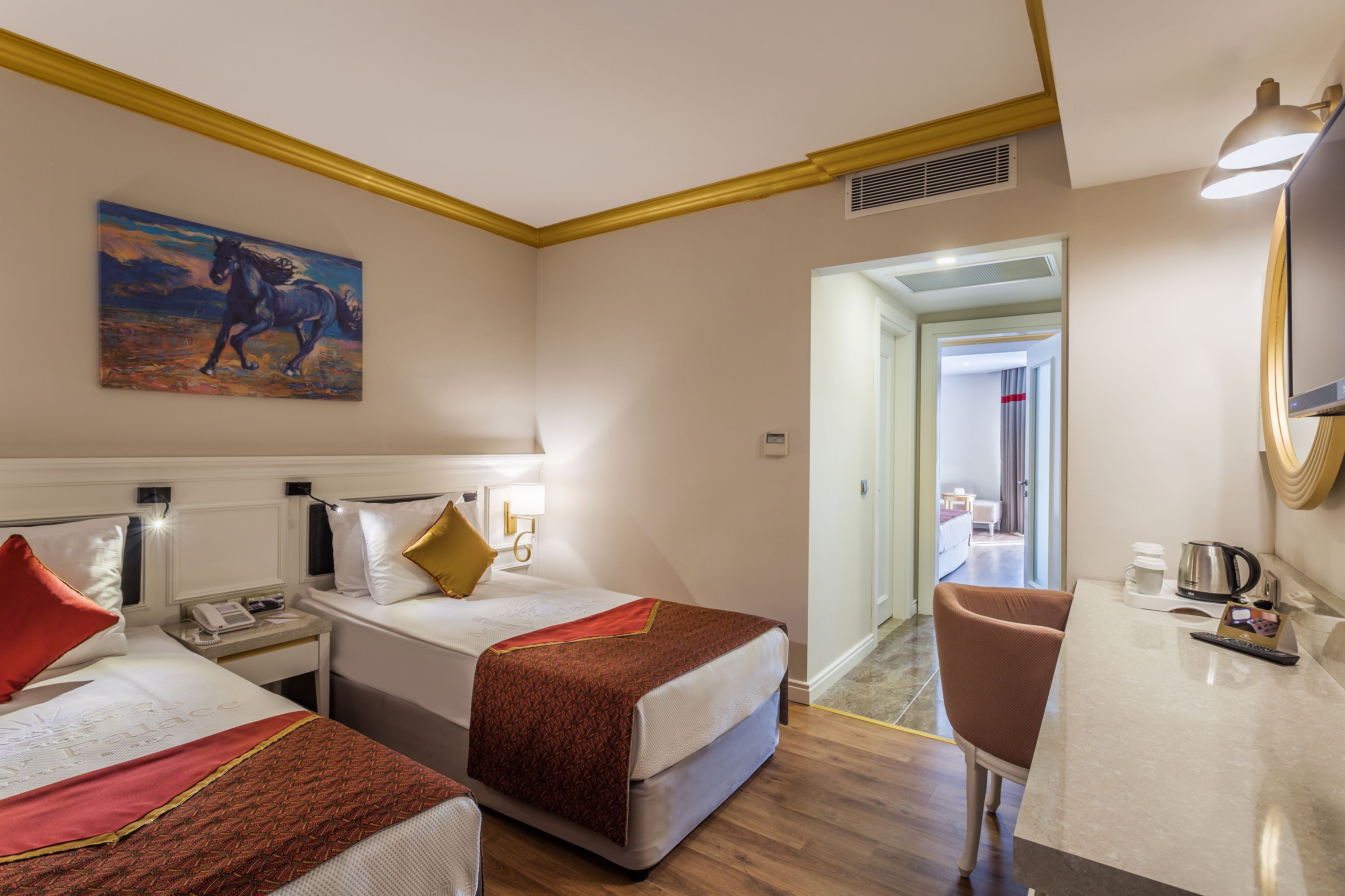 Une chambre d’hôtel avec deux lits, un bureau, une chaise, un tableau et une vue sur le couloir.