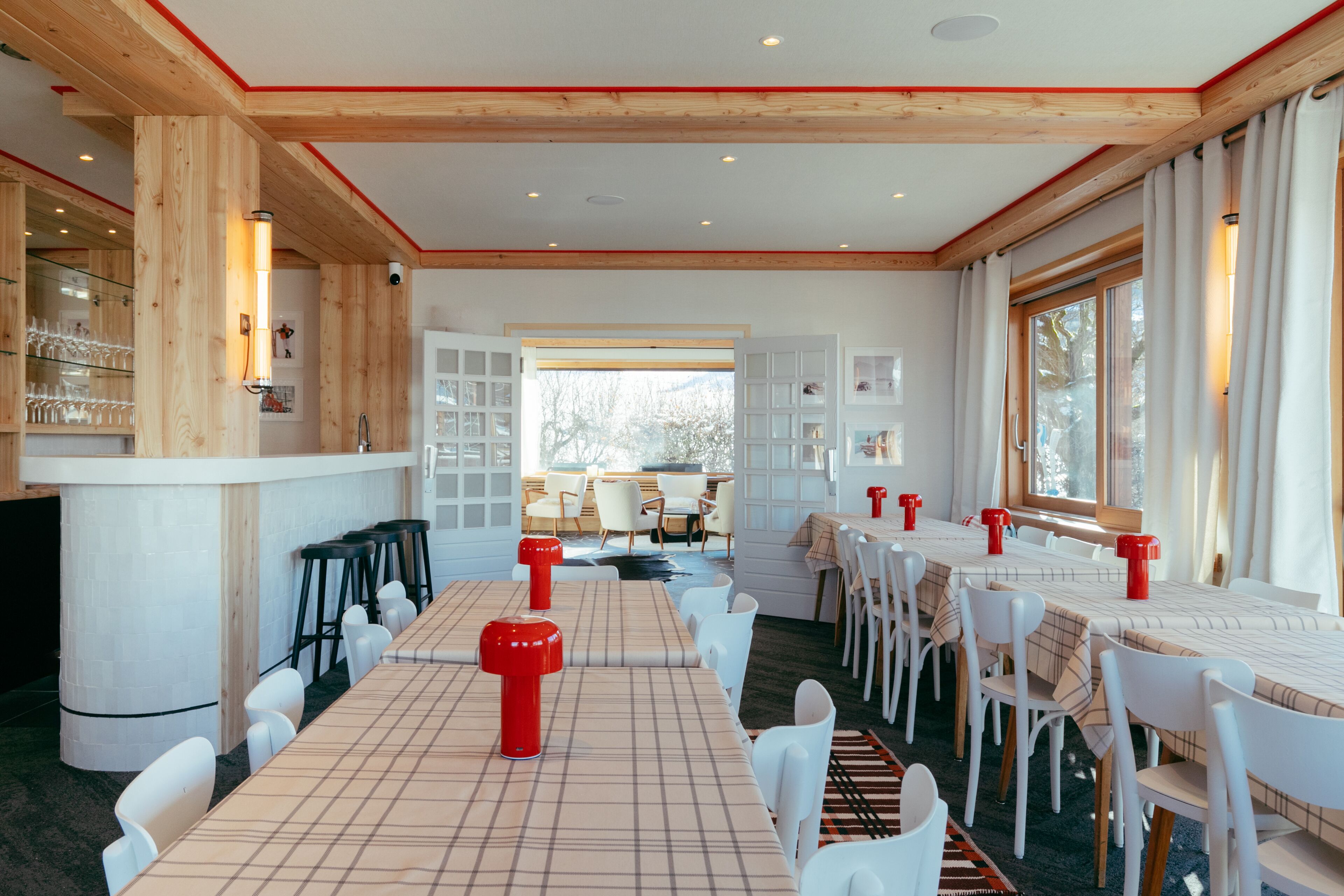 A spacious dining area with long tables, white chairs, and red candle holders.