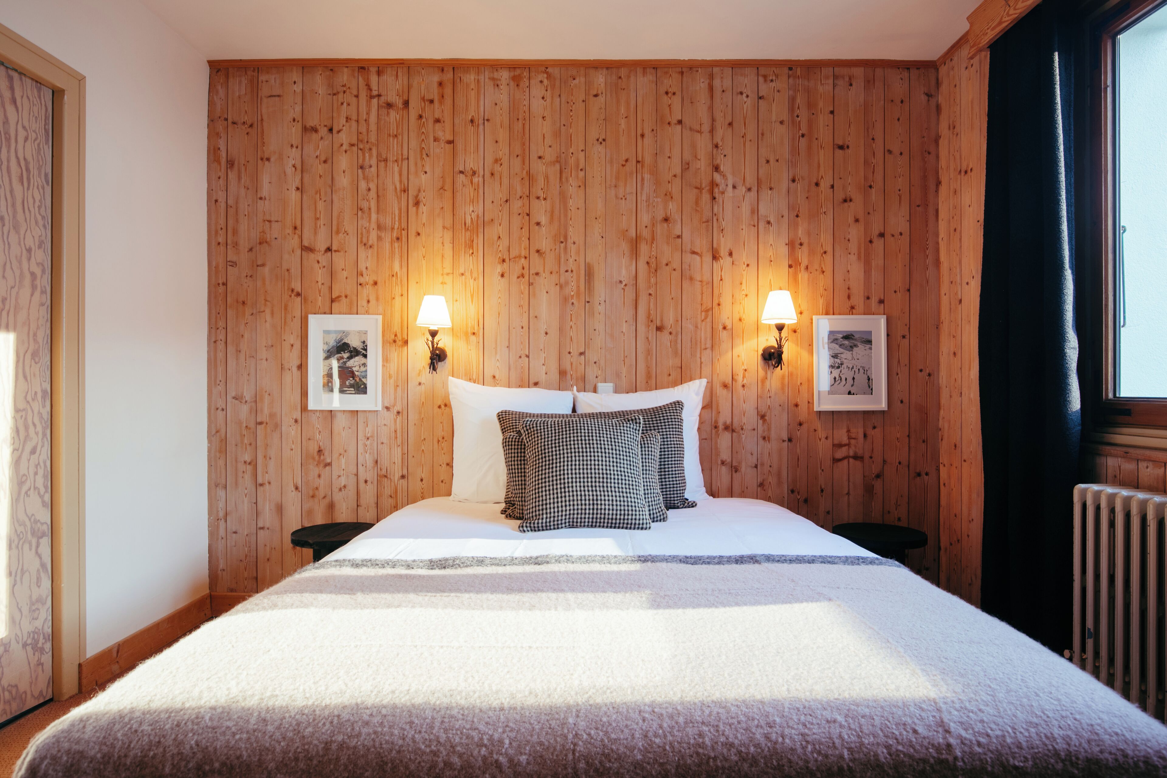 Un dormitorio con paneles de madera, una cama con ropa de cama blanca, dos lámparas de noche y cuadros enmarcados en la pared.