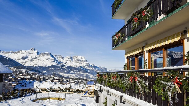A hotel with balconies decorated with greenery and red bows, overlooking a snowy mountain landscape. - Caprice Des Neiges (Combloux)