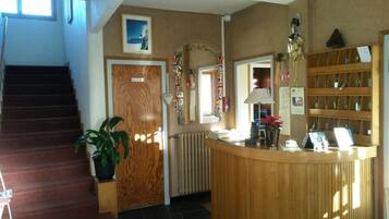 A reception area with a wooden desk, a reception counter, a staircase, a potted plant, and a framed picture on the wall.