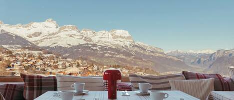 A table set for two with a view of snow-capped mountains and a village in the background.