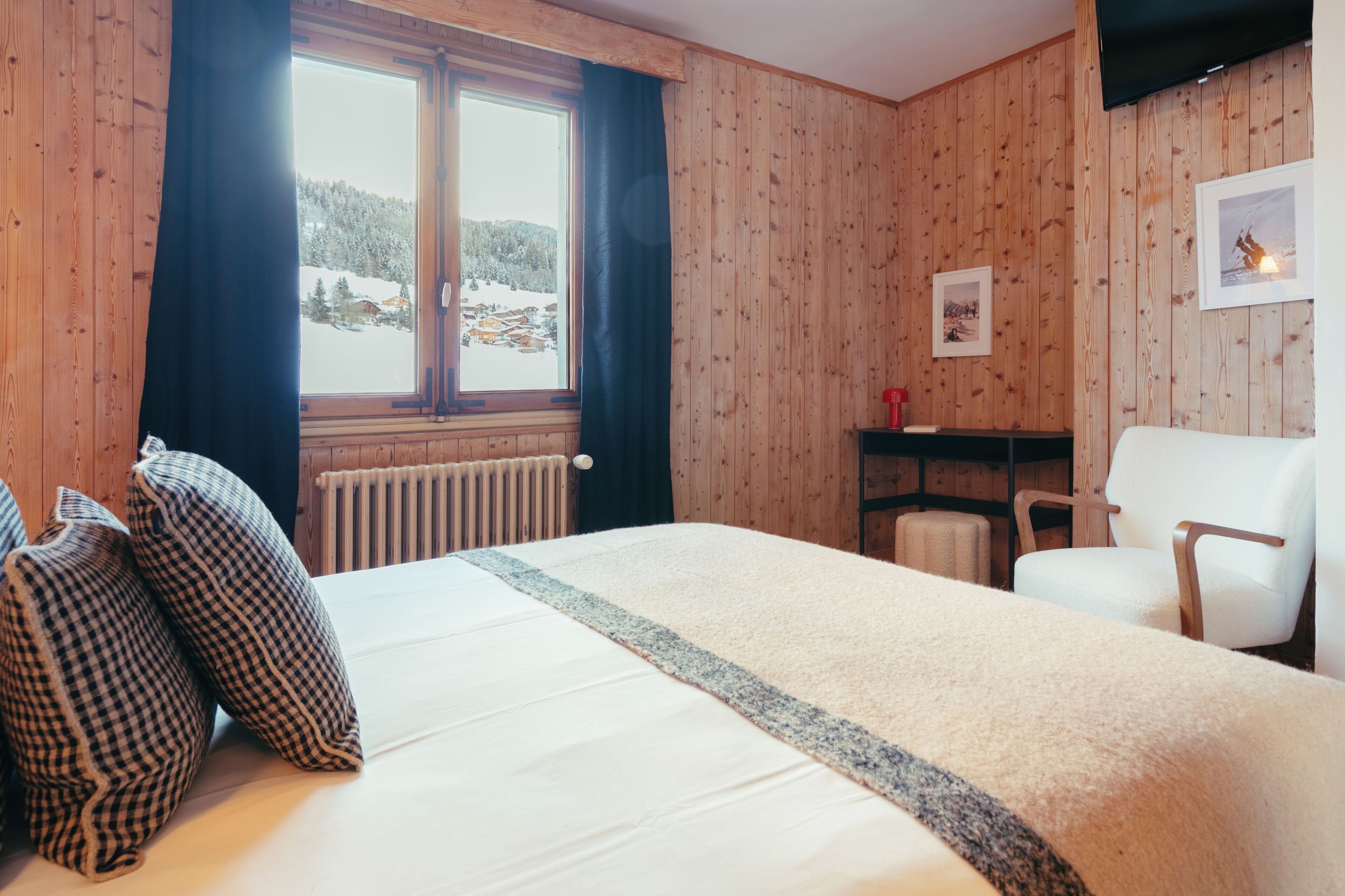A wooden-paneled room with a bed, a chair, a radiator, and a window with curtains.