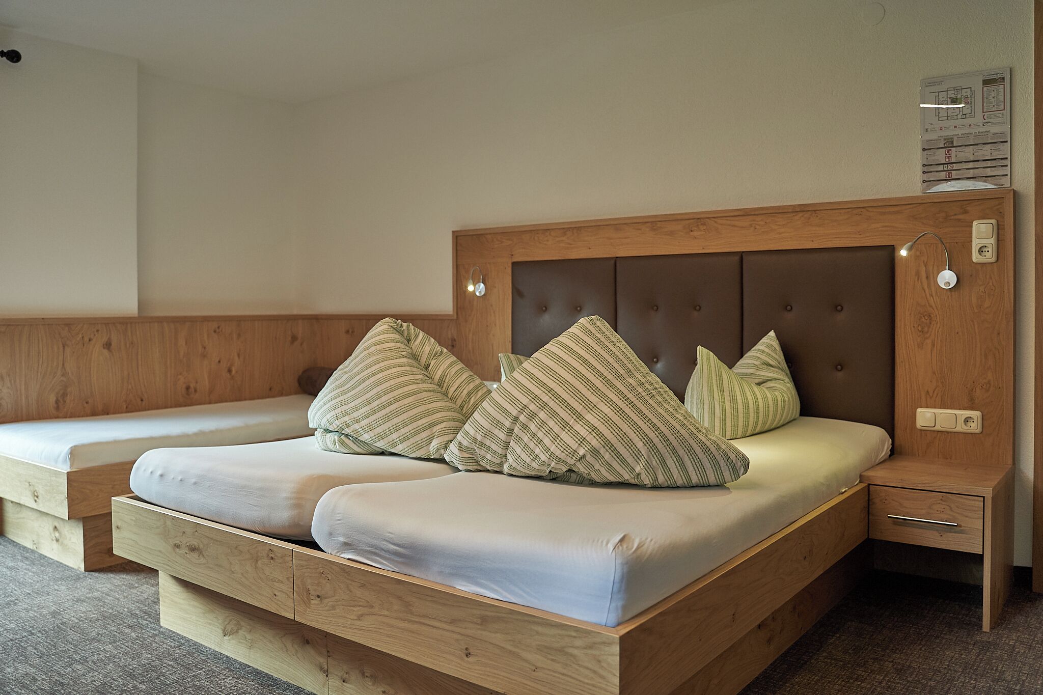 A wooden bed with a headboard, two pillows, a bedside table, and a nightstand.