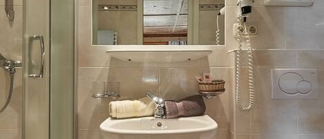 Une salle de bain avec une douche à parois de verre, un lavabo avec un miroir au-dessus, un sèche-cheveux fixé au mur et une baignoire.