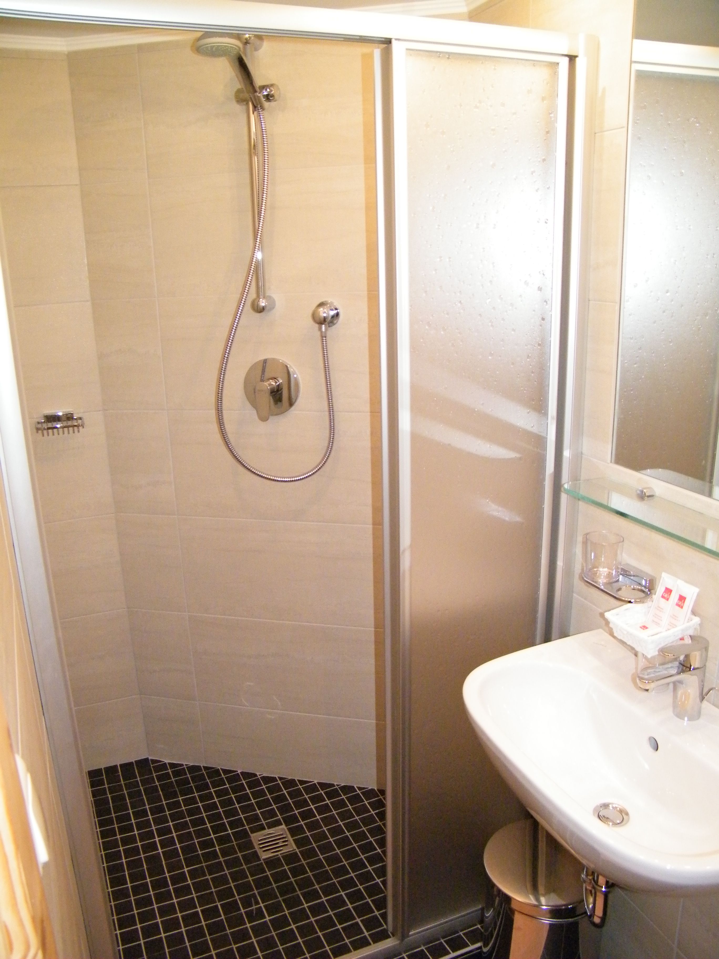 A bathroom with a glass shower enclosure, a white sink, and a mirror above the sink.