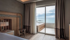 A hotel room with a bed, a bedside table with a lamp, a small table, a wooden bench, and a view of the sea through a sliding glass door. - Adalya Bliss - All inclusive (Manavgat)