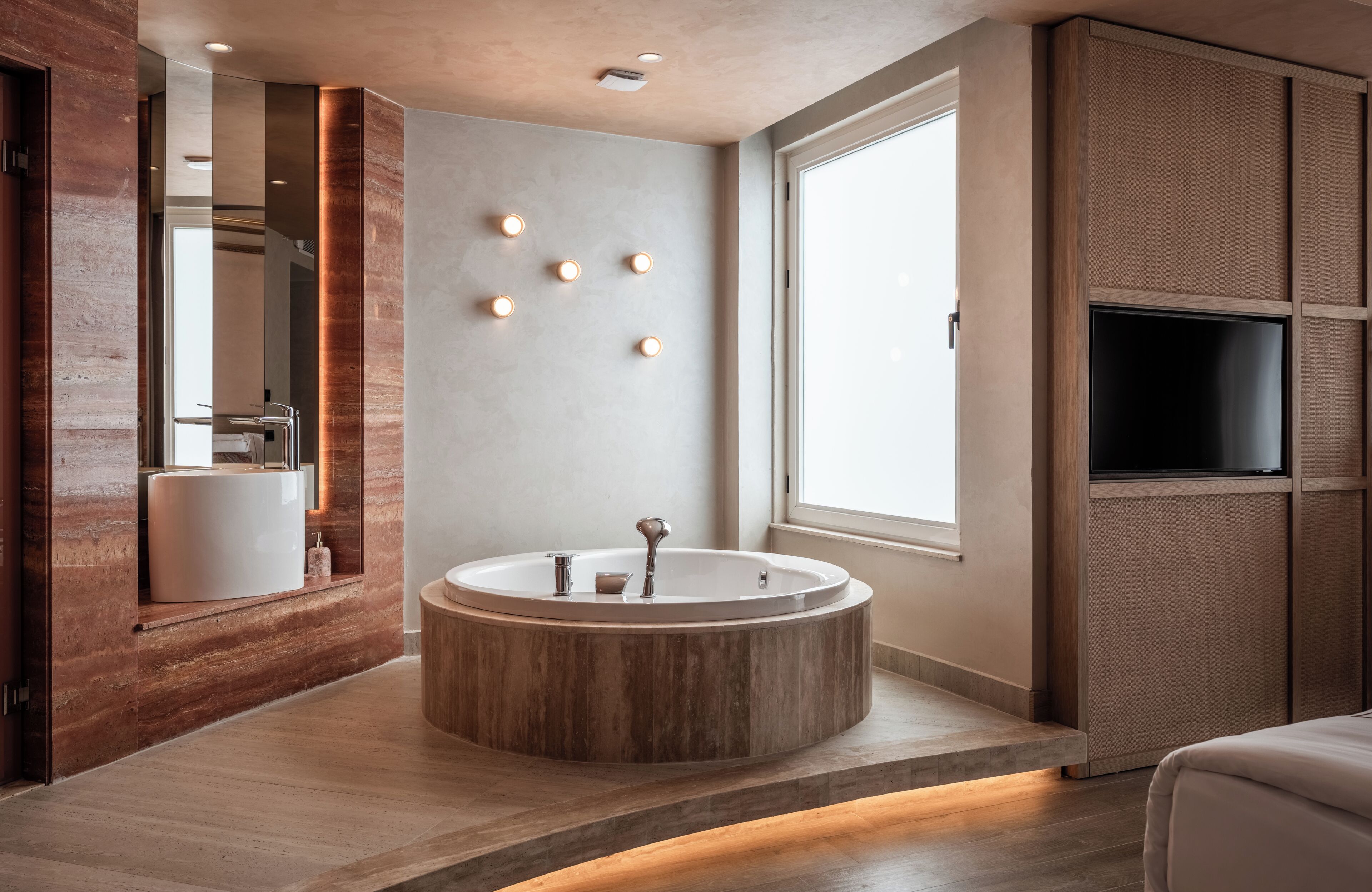 A modern bathroom with a freestanding bathtub, a large mirror, and a television mounted on the wall.