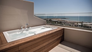 A modern bathroom with a wooden vanity, a large bathtub, and a glass-enclosed balcony with a view of the sea and buildings. - Adalya Bliss - All inclusive (Manavgat)