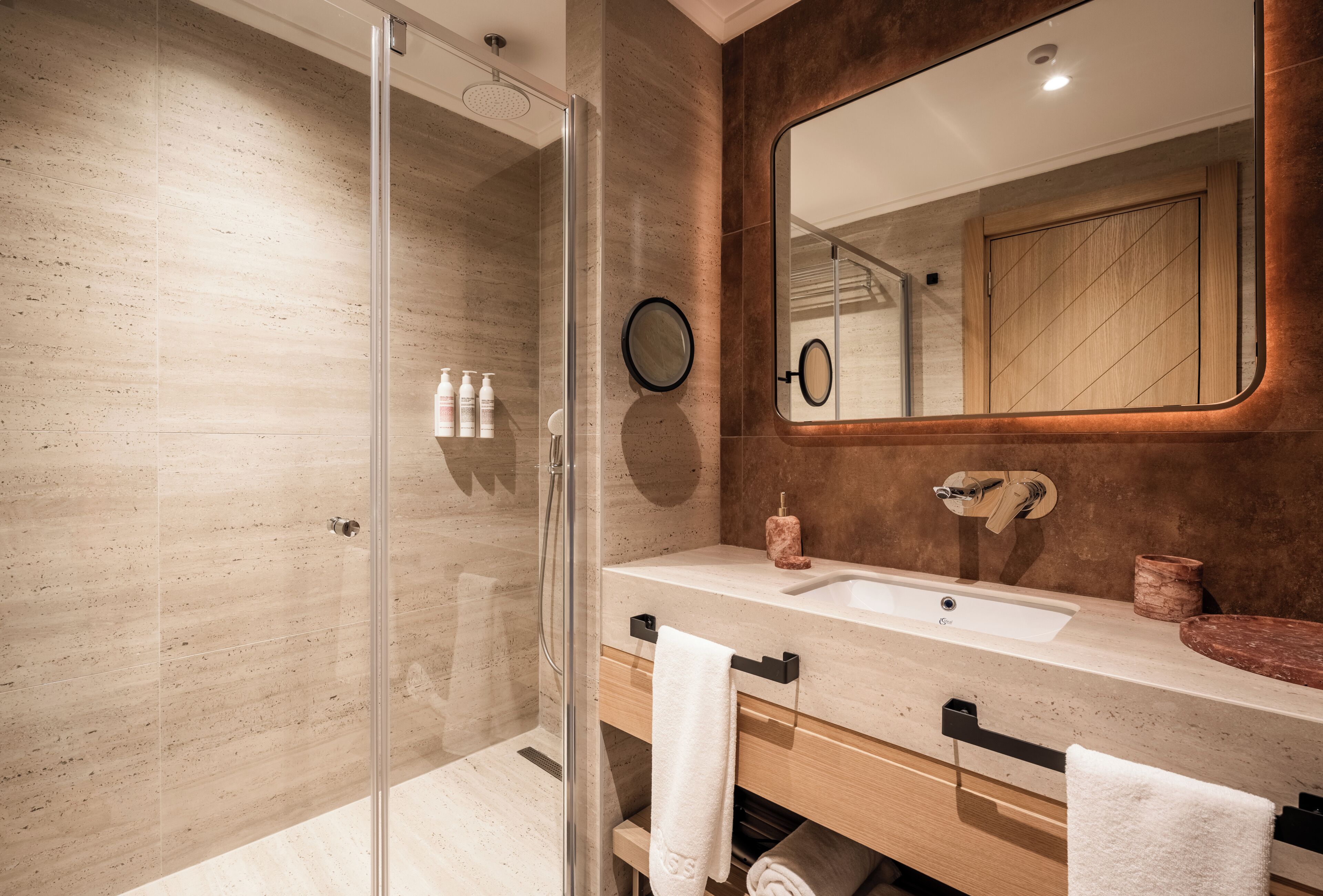 A modern bathroom with a glass shower enclosure, a sink with a wooden vanity, and a large mirror.