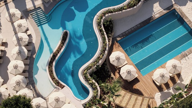 A pool with a wavy edge, surrounded by umbrellas and lounge chairs. - Adalya Bliss - All inclusive (Manavgat)