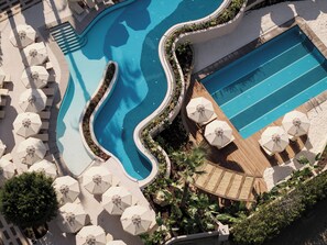 Una piscina con borde ondulado, rodeada de sombrillas y sillones de descanso.