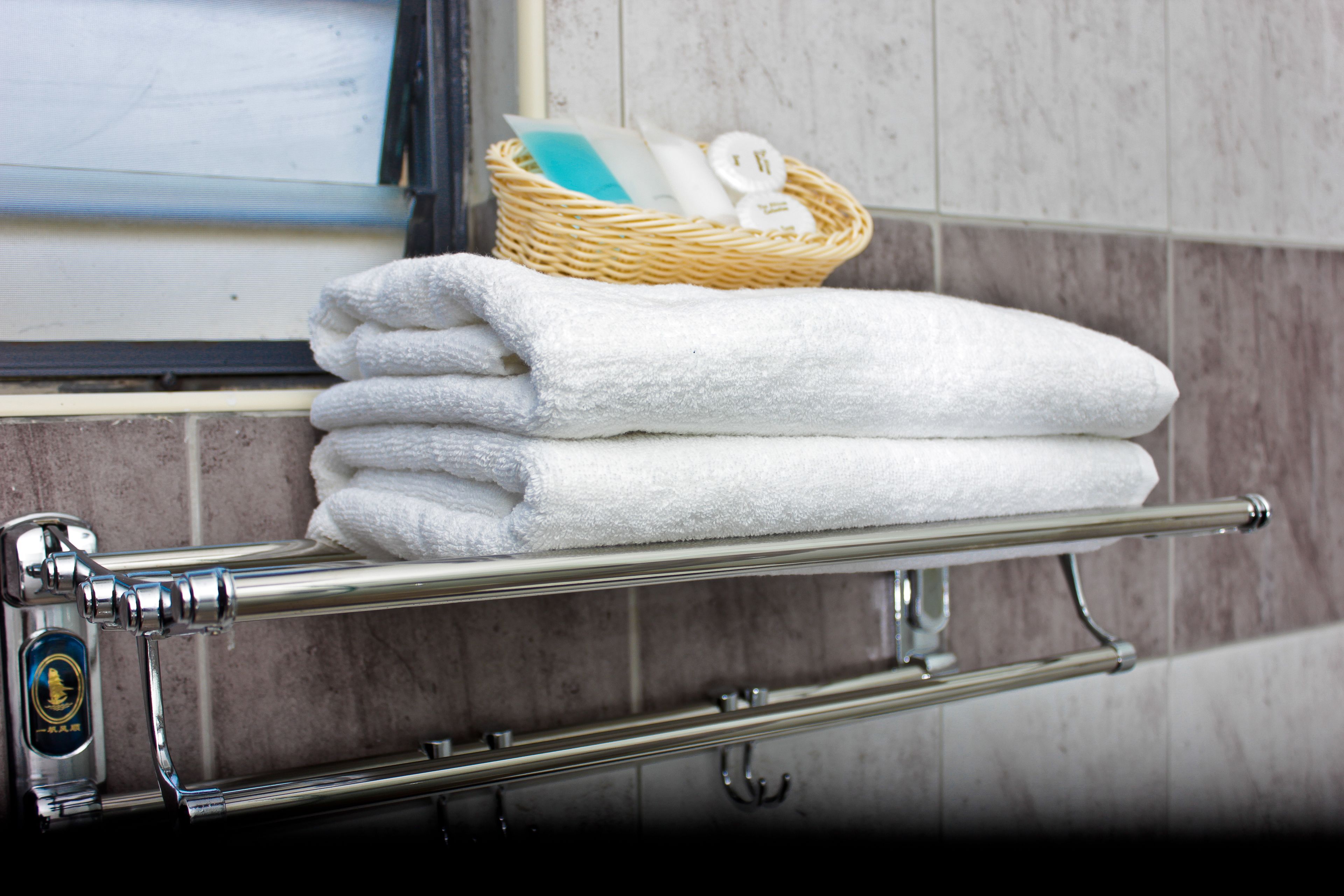 A bathroom with a towel rack holding neatly folded white towels and a wicker basket containing toiletries.