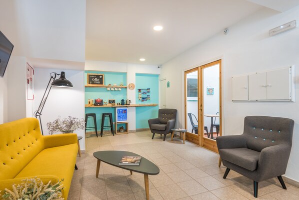 A modern living room with a yellow sofa, a grey armchair, a coffee bar, and a small table with a magazine. - Hostal Jume - Urban Rooms (Mahón)