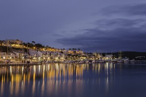 Un puerto deportivo con barcos amarrados, edificios a lo largo del muelle y aguas tranquilas que reflejan las luces.