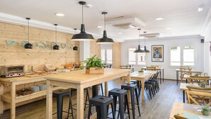Un restaurante moderno con mesas de madera y taburetes de bar negros, una barra larga con una planta e iluminación colgante.