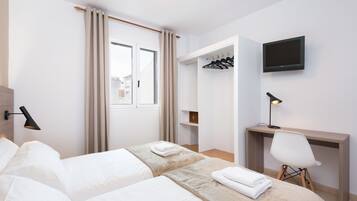 Habitació d'hotel amb dos llits, un escriptori, una cadira, un televisor i un armari.