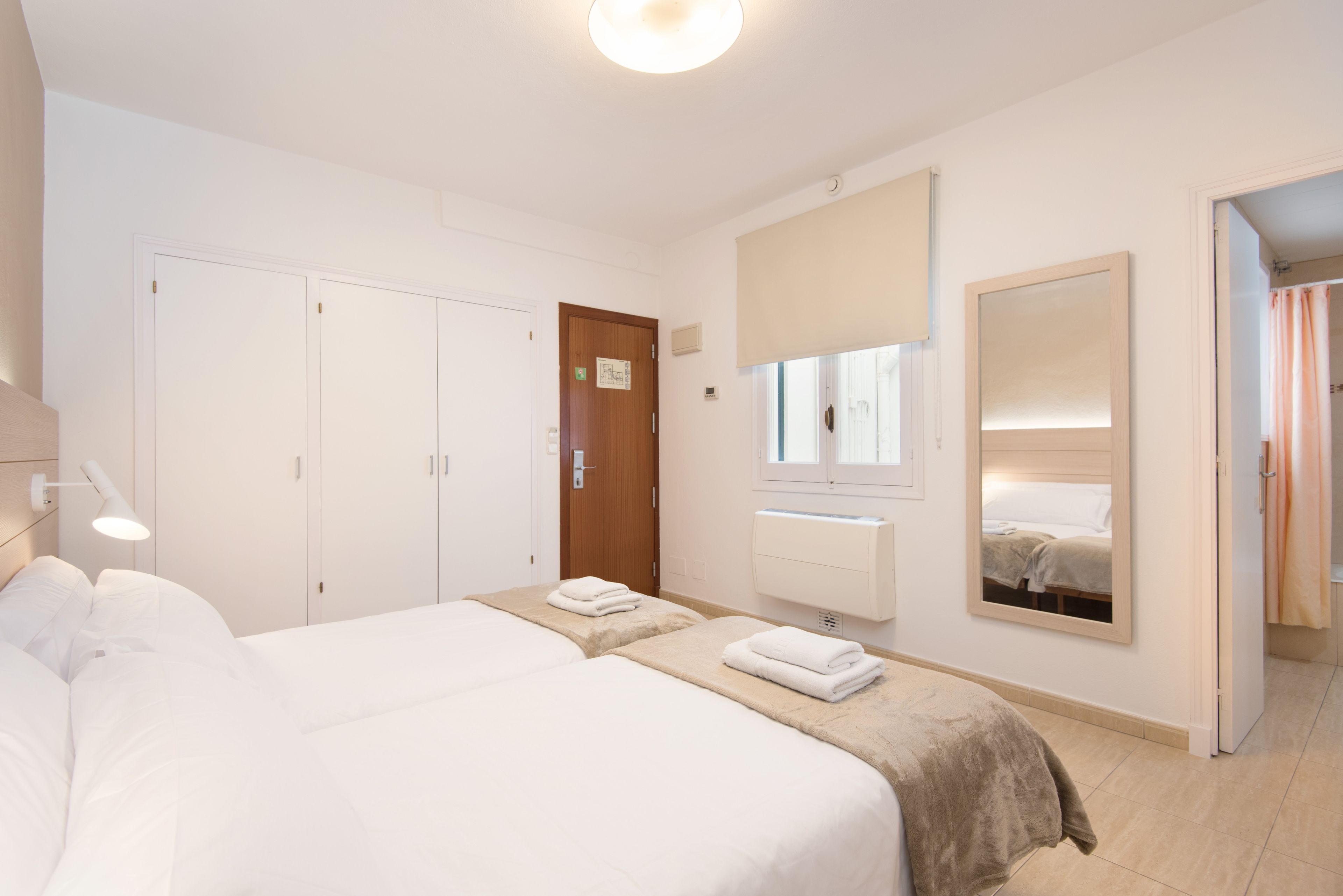 A hotel room with two beds, a large mirror, a wardrobe, and a bathroom visible through an open door.