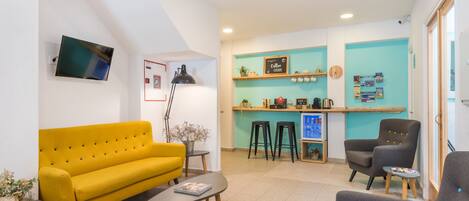 A modern living area with a yellow sofa, a coffee bar, and a TV mounted on the wall.