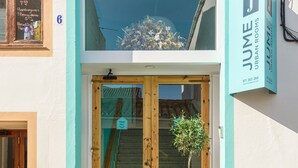 Entrada de hotel con puerta de madera, una planta en maceta y un letrero que dice 'JUNE URBAN ROOMS'.