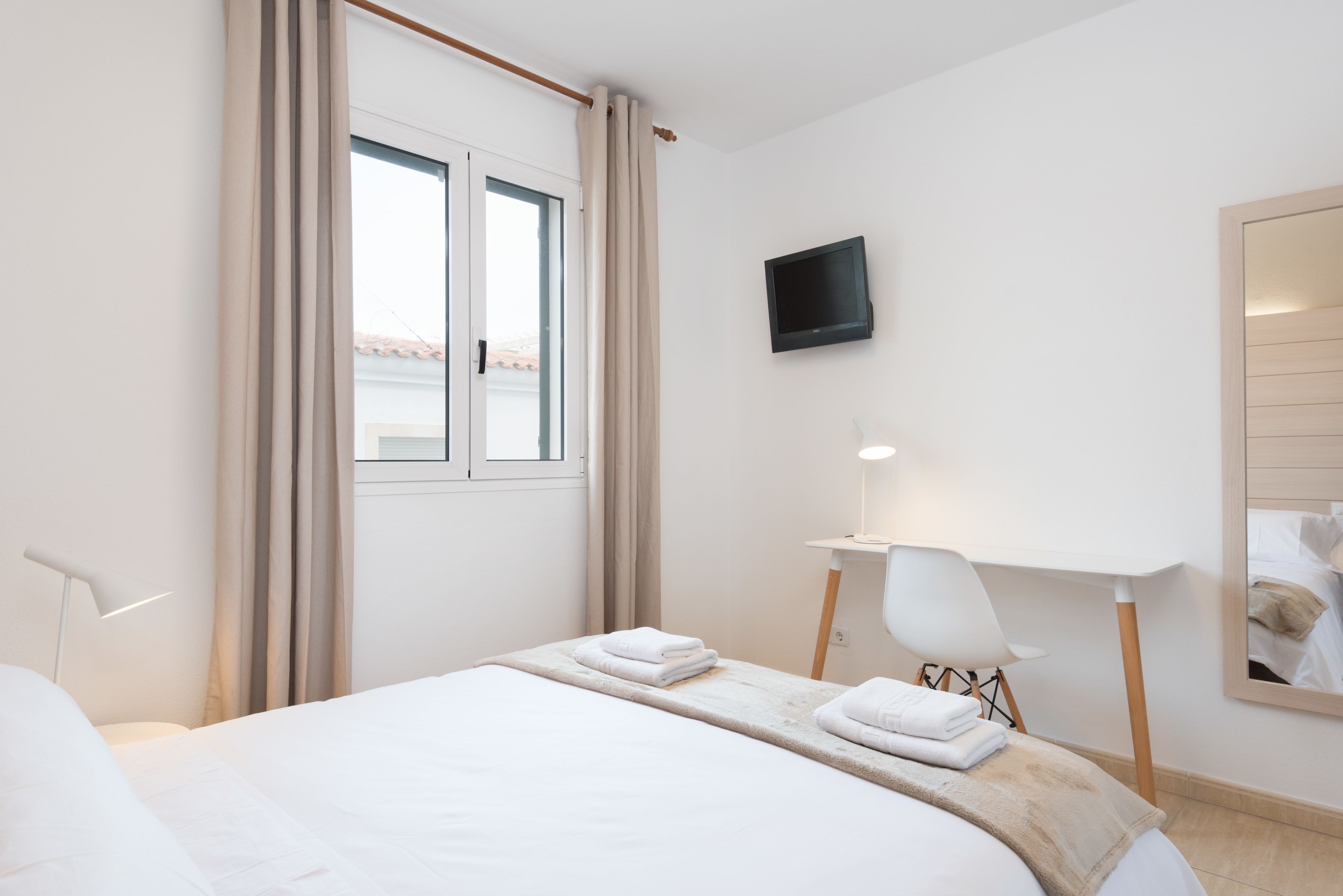 Habitación de hotel con cama, televisión montada en la pared, escritorio con silla y ventana con cortinas.