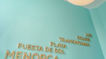A wall with wooden letters spelling "PUESTA DE SOL MENORCA" and "TRAMONTANA" in a hotel room.