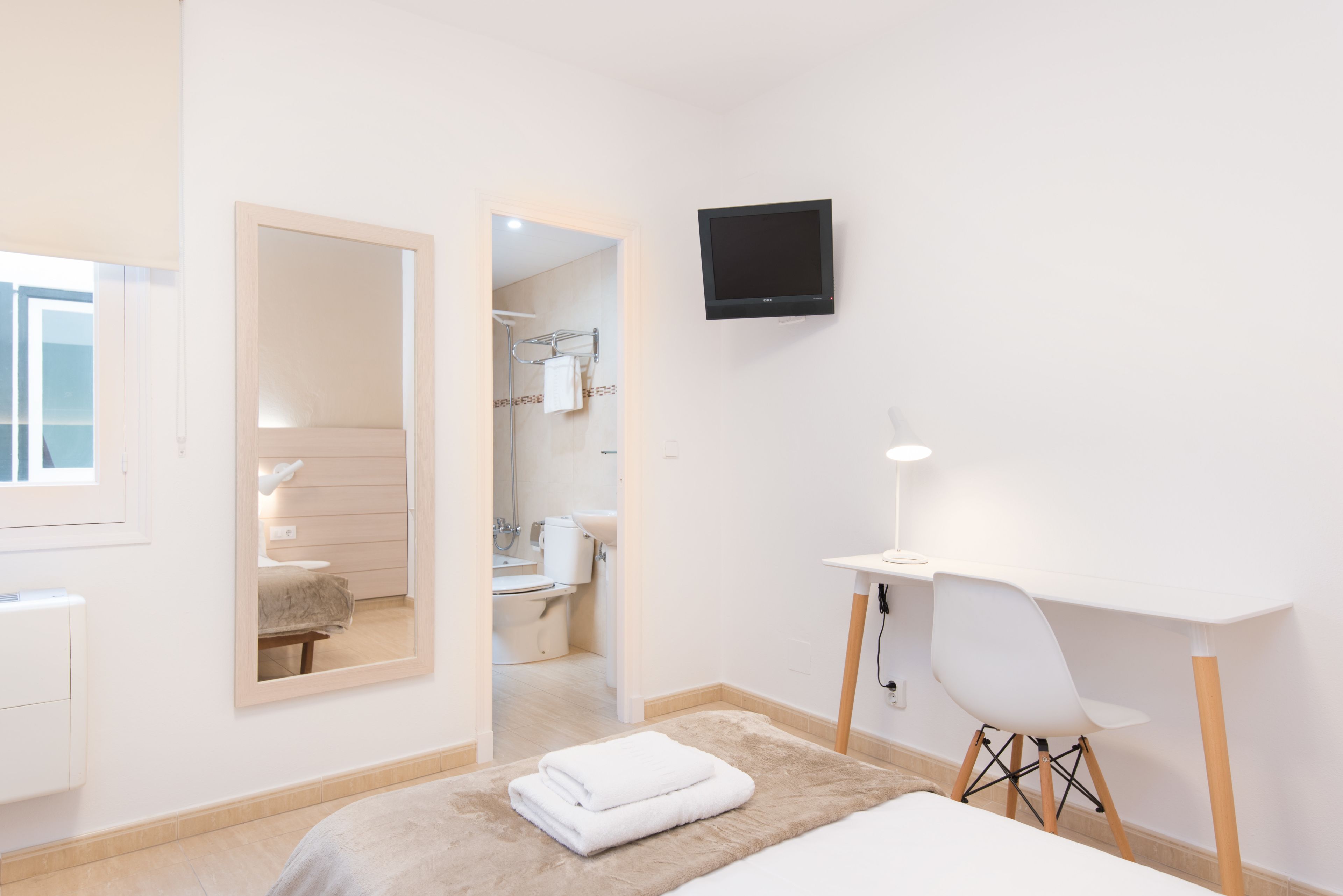 Habitación de hotel moderna con cama, escritorio, silla, televisión y baño visible a través de una puerta abierta.