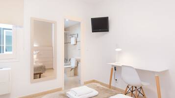 Une chambre d’hôtel moderne équipée d’un lit, d’un bureau, d’une chaise, d’une télévision et d’une salle de bain visible à travers une porte ouverte.