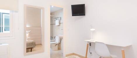 Habitación de hotel moderna con cama, escritorio, silla, televisión y baño visible a través de una puerta abierta.