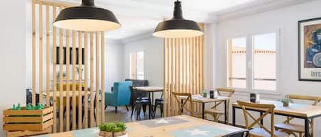 Un comedor moderno con mesas y sillas de madera, iluminación colgante y vistas al exterior.