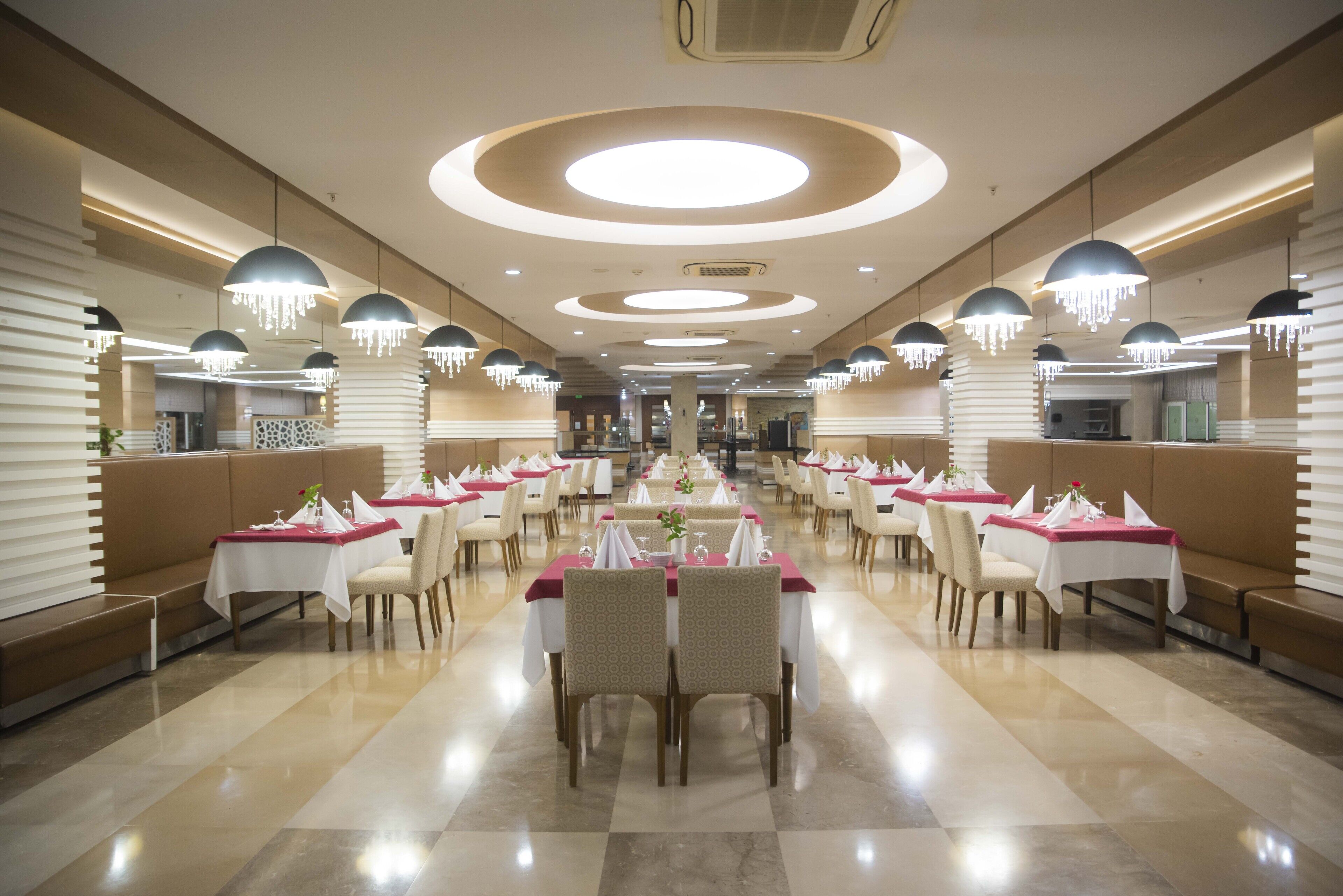 Un comedor amplio con varias mesas y sillas, con un diseño moderno que incluye luces de techo circulares y colgantes.