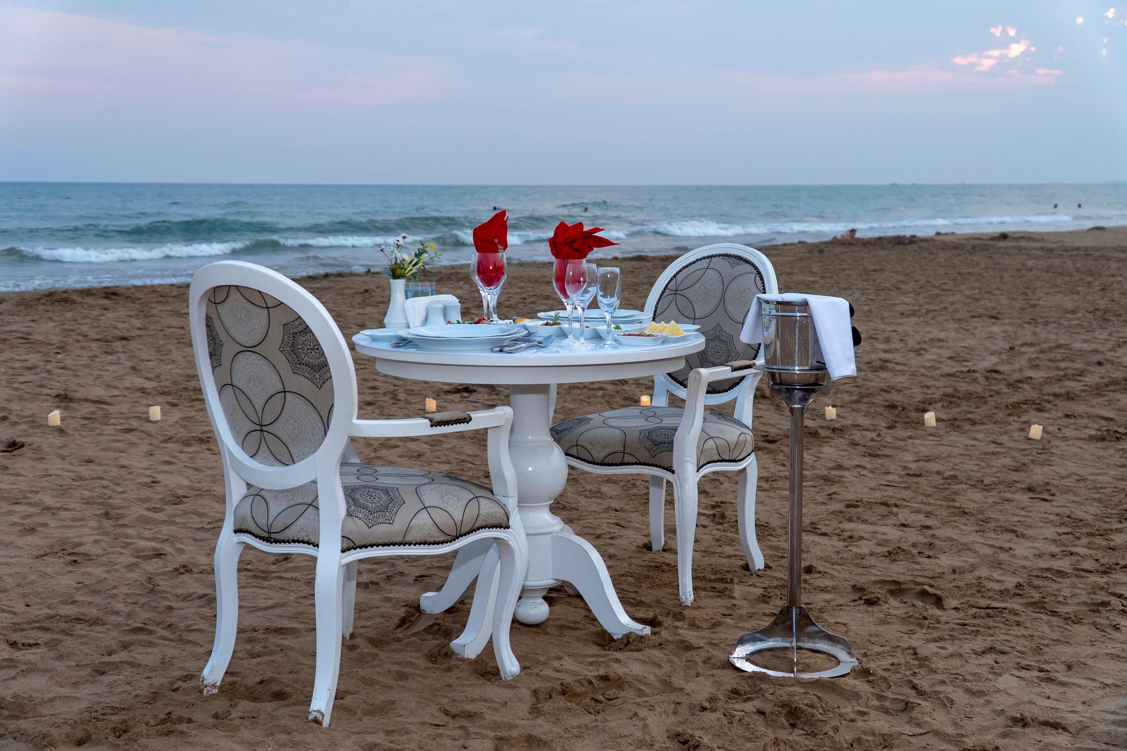 A table set for two on a sandy beach with ocean views.